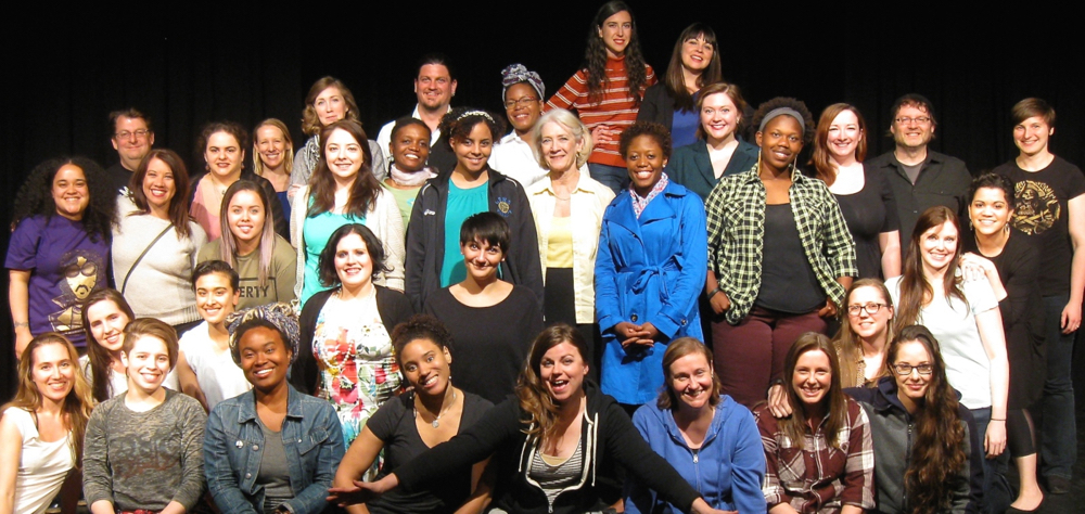 A large group of artists of different ethnicities in contemporary casual dress gather on a stage, smiling at the camera