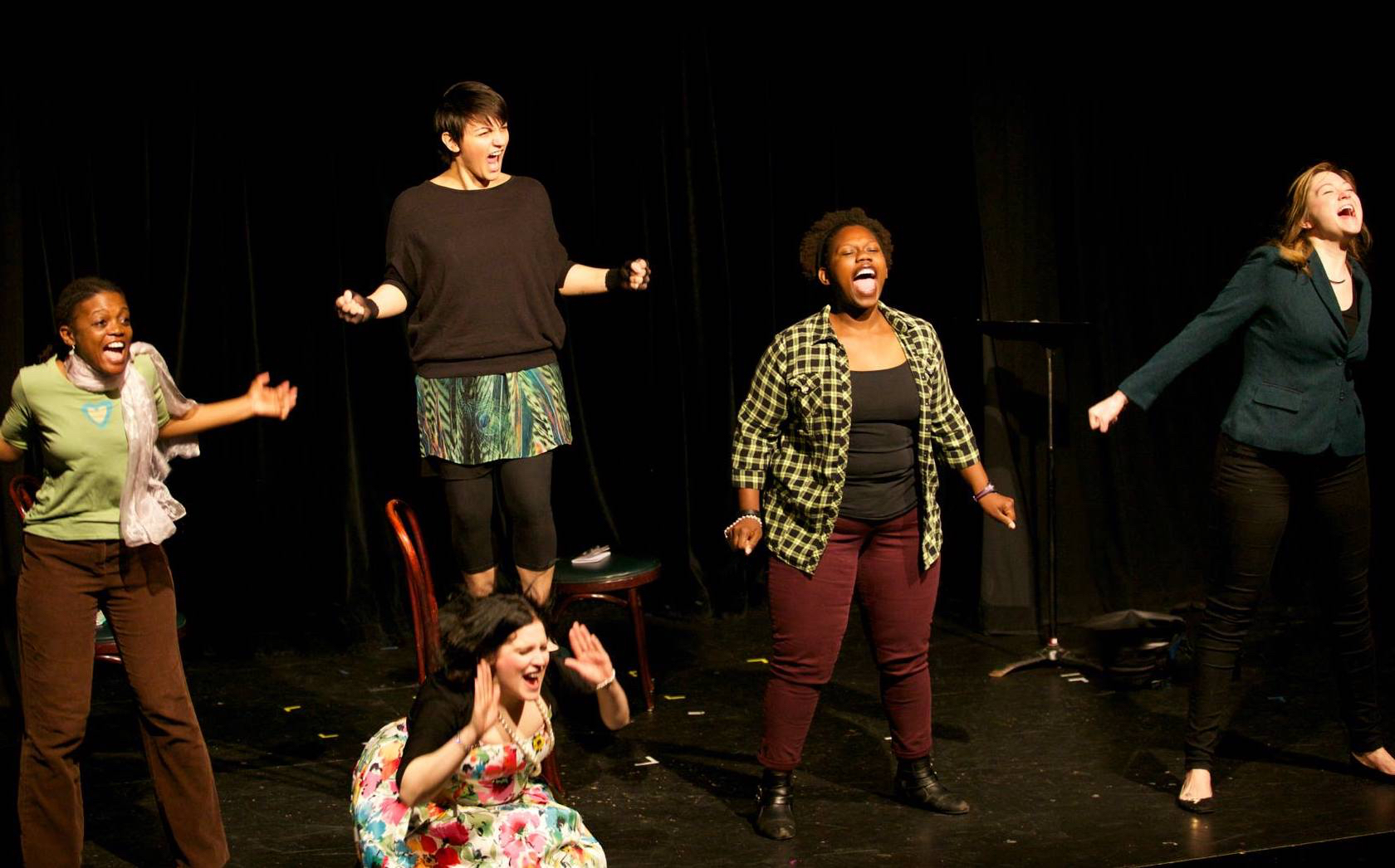 Five women on a stage enthusiastically exclaim