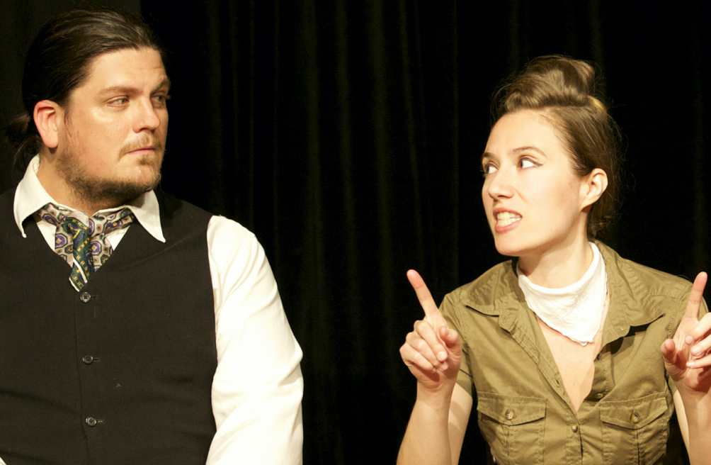 Two characters, who appear to be a man wearing an ascot and a women wearing a white handkerchief as a scarf, look intensely at each other.