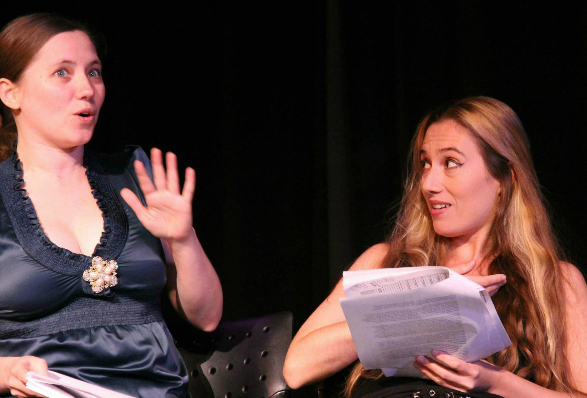 Two women actors hold scripts and act on stage