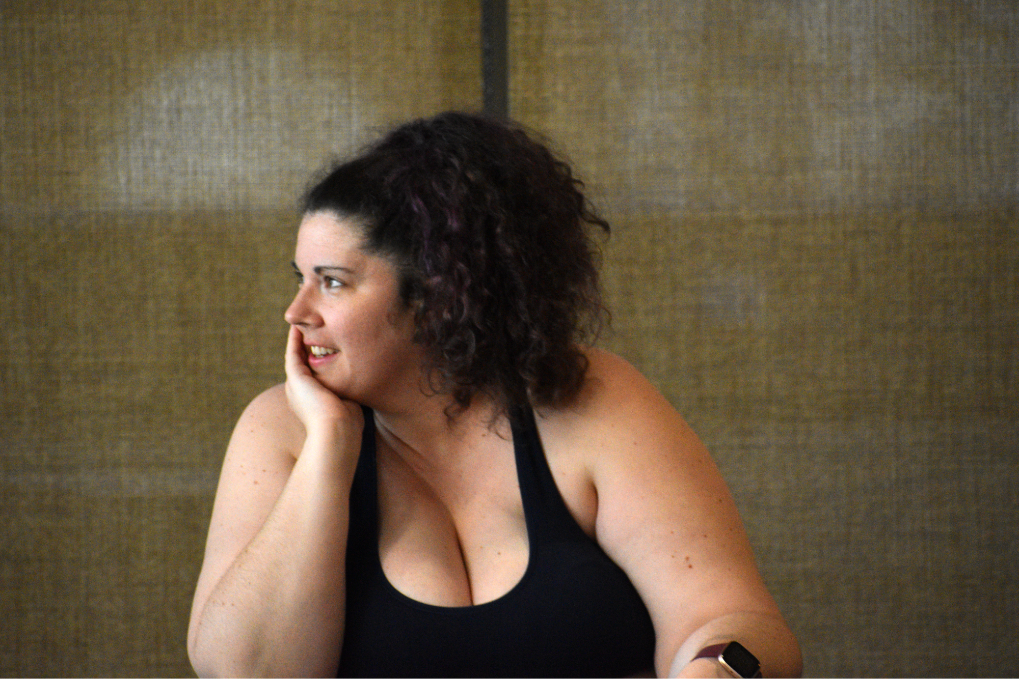 Eileen Tull sitting on stage wearing a black tank top, her hand is on her chin and she is smiling.

